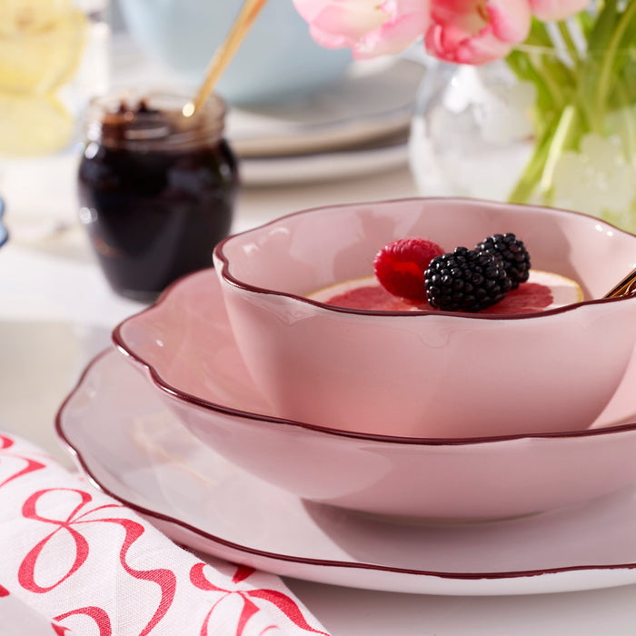 Pink ceramic bowl with berries on a table setting with a floral napkin and jam jar.
