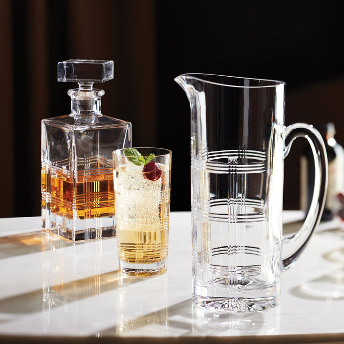 Clear glass decanter, pitcher, and cocktail on a reflective surface with a dark background