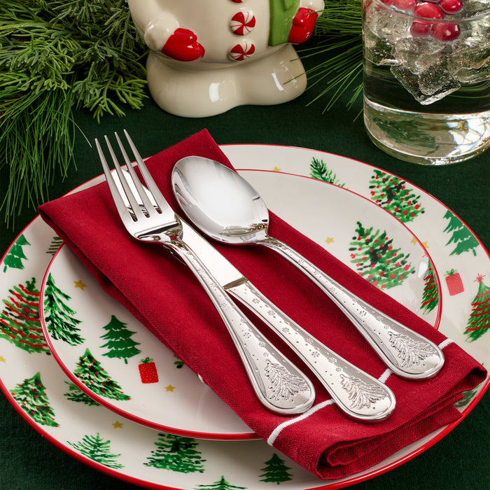 Christmas-themed table setting with silverware on a plate with tree patterns.